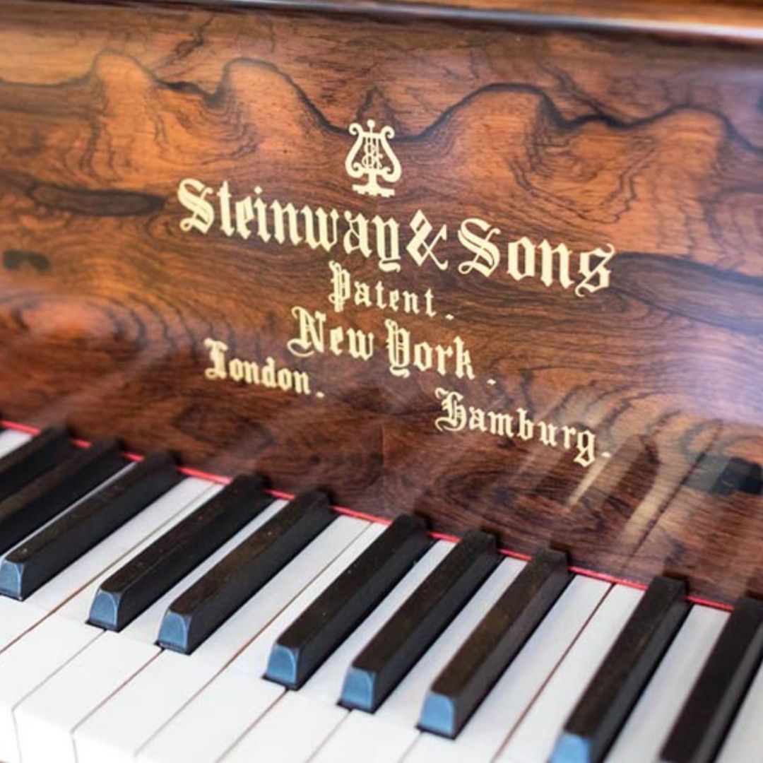 The fallboard of an old Steinway grand piano with its wordmark in fancy lettering and a unique wood finish.