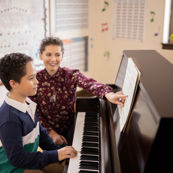 Upright piano being used in a piano lesson with a young student and an encouraging teacher pointing to sheet music.